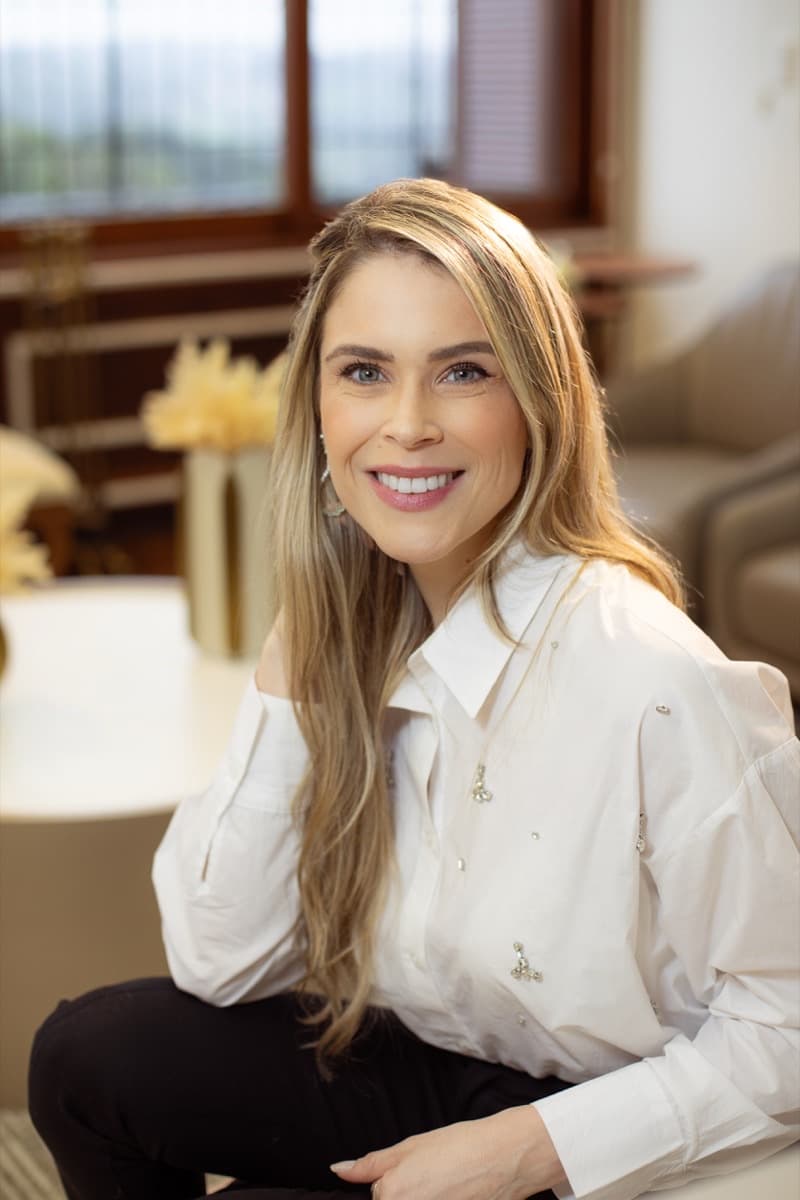 Dra. Luíse Pezzin sorrindo em ambiente de consultório com decoração em tons claros